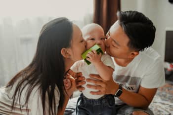 A joyful family scene with parents affectionately kissing their baby indoors, showcasing love and togetherness.