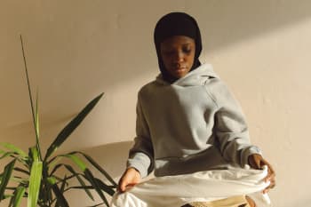 Contemplative young woman wearing hijab and hoodie sitting indoors in natural light.